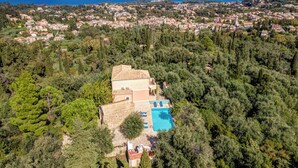 Luftaufnahme einer Küstenstadt mit einer markanten Villa, einem Pool und üppiger Vegetation.