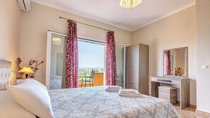 Ein Schlafzimmer mit Bett, Schreibtisch, Stuhl, Spiegel und einem Balkon mit Vorhängen.