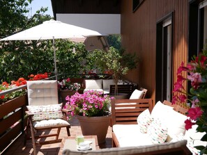 An outdoor seating area with wooden furniture, a large potted plant with pink flowers, and a white umbrella. - Room 'Doppelzimmer - Nr 4' with Shared Terrace, Shared Garden and Balcony (Dachsberg)