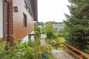 Un edificio residenziale con facciata in mattoni, una scala in legno e un giardino con piante diverse e un grande albero sempreverde.