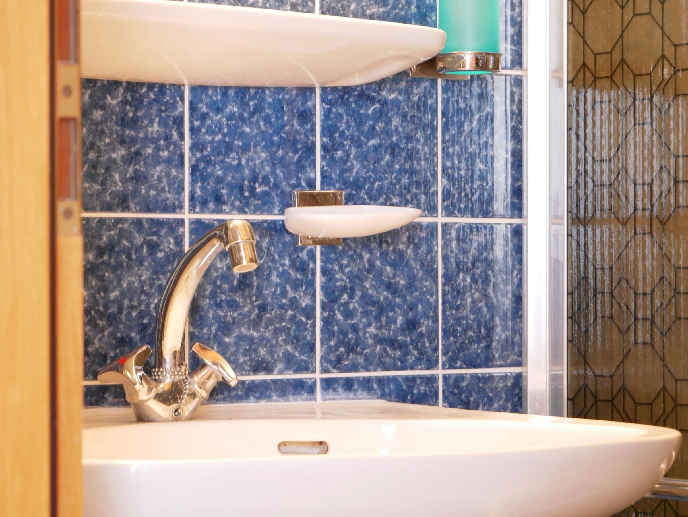 A bathroom with a white sink, a chrome faucet, and blue speckled tiles.