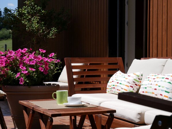 A wooden outdoor seating area with a table, a chair, and a sofa with patterned cushions. - Apartment 'No. 3' with Shared Terrace, Shared Garden and Balcony (Dachsberg)