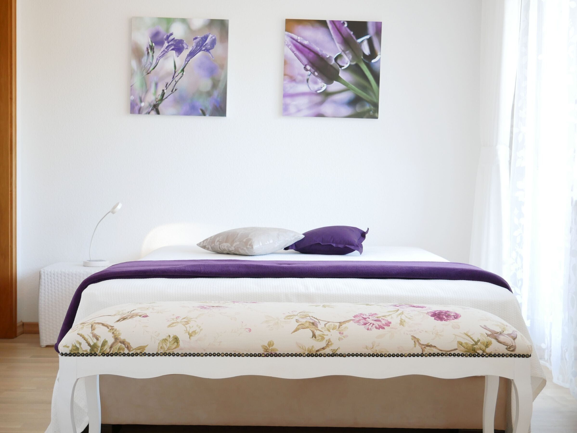 A bed with a floral bedspread, a white headboard, and two wall-mounted floral paintings.