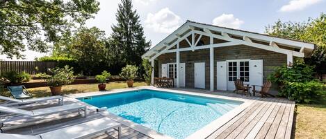 A wooden deck with a swimming pool, a covered patio, and a fenced yard.