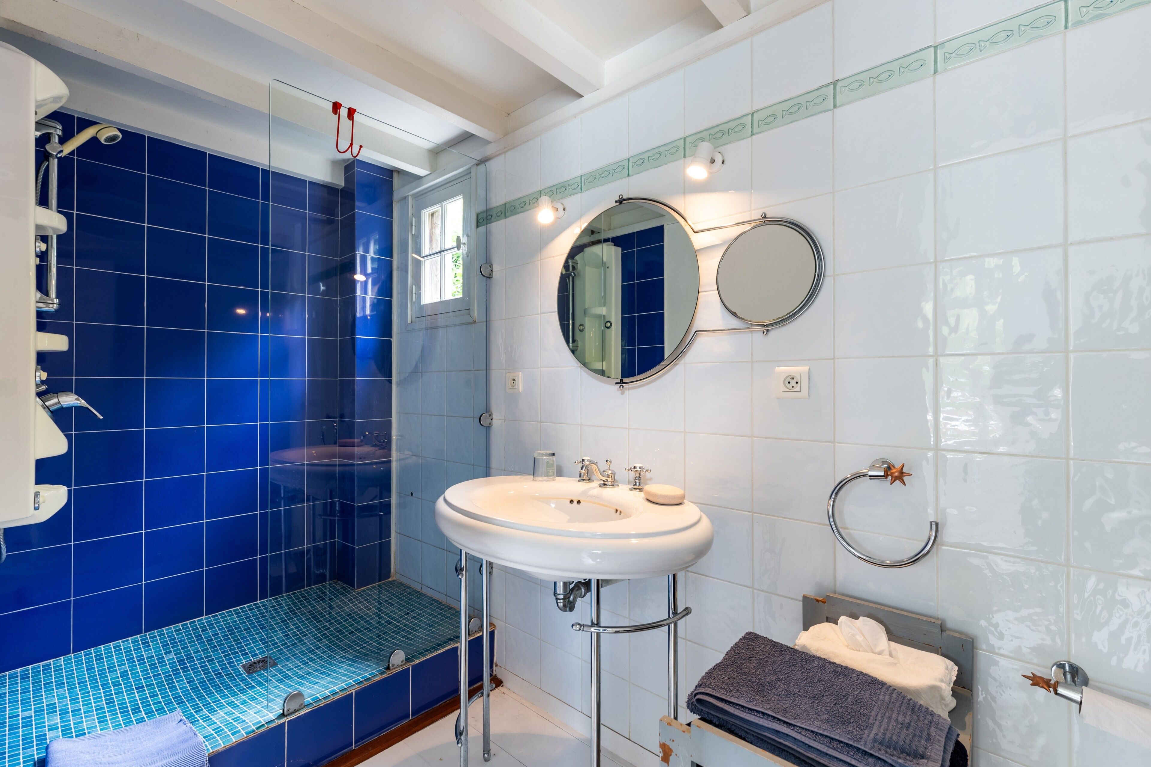 A bathroom with a blue-tiled shower, a white sink with a mirror, and a towel rack.