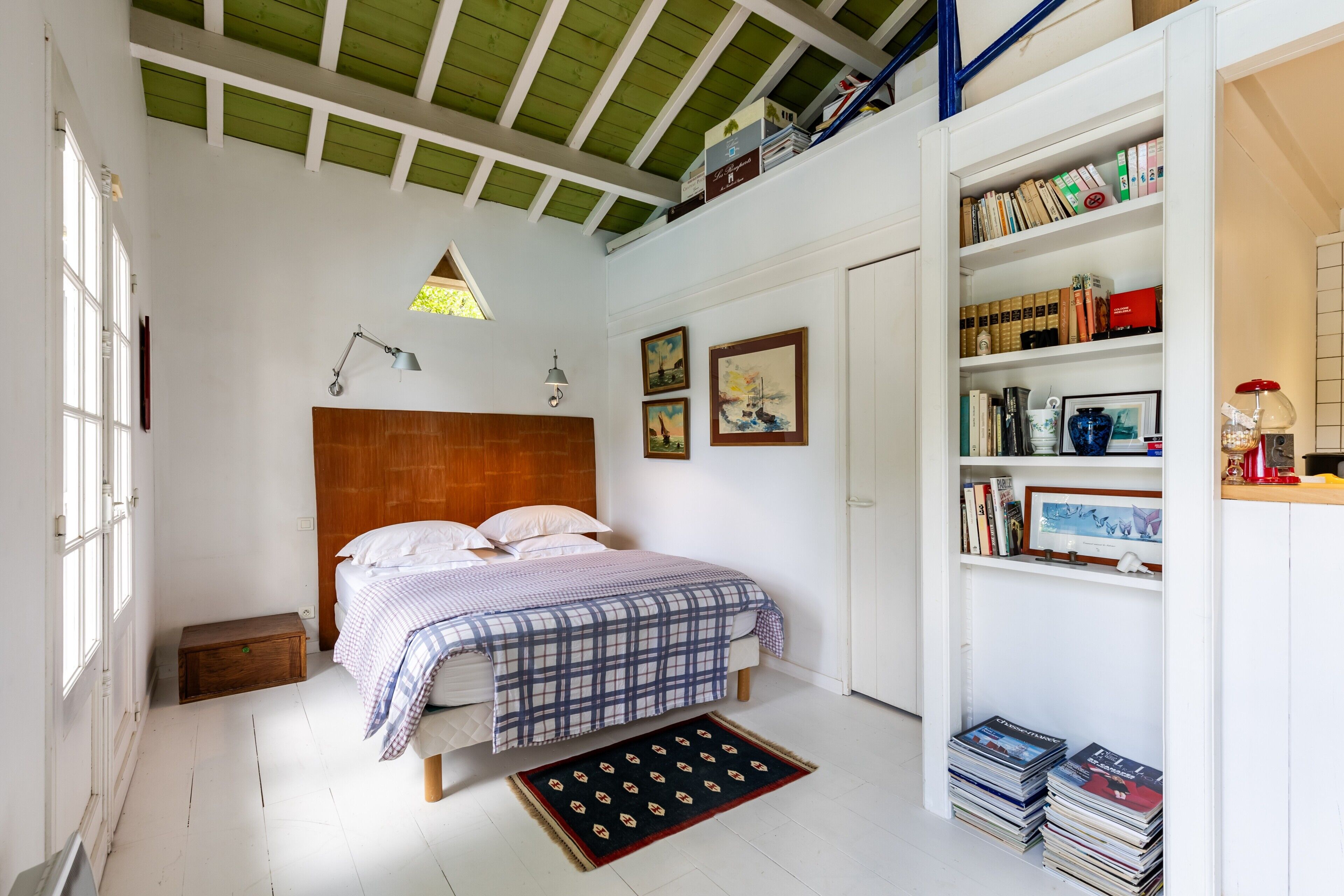 Un dormitorio con cama, estantería, escritorio y ventana.