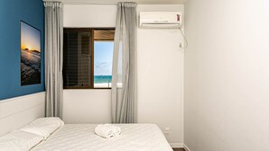 Una camera da letto con un letto, una finestra vista mare, un condizionatore e un quadro appeso al muro.