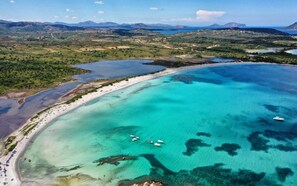 An aerial view of a coastal area with clear turquoise waters, a sandy beach, and boats.