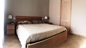 A bedroom with a wooden bed, two bedside tables, a nightstand, a door, and a wall switch. - Apartment 'Florida 2' with Sea View, Wi-Fi and Air Conditioning (San Teodoro)
