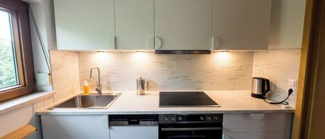 A compact kitchen with white cabinets, a built-in dishwasher, a stove, and a coffee maker.