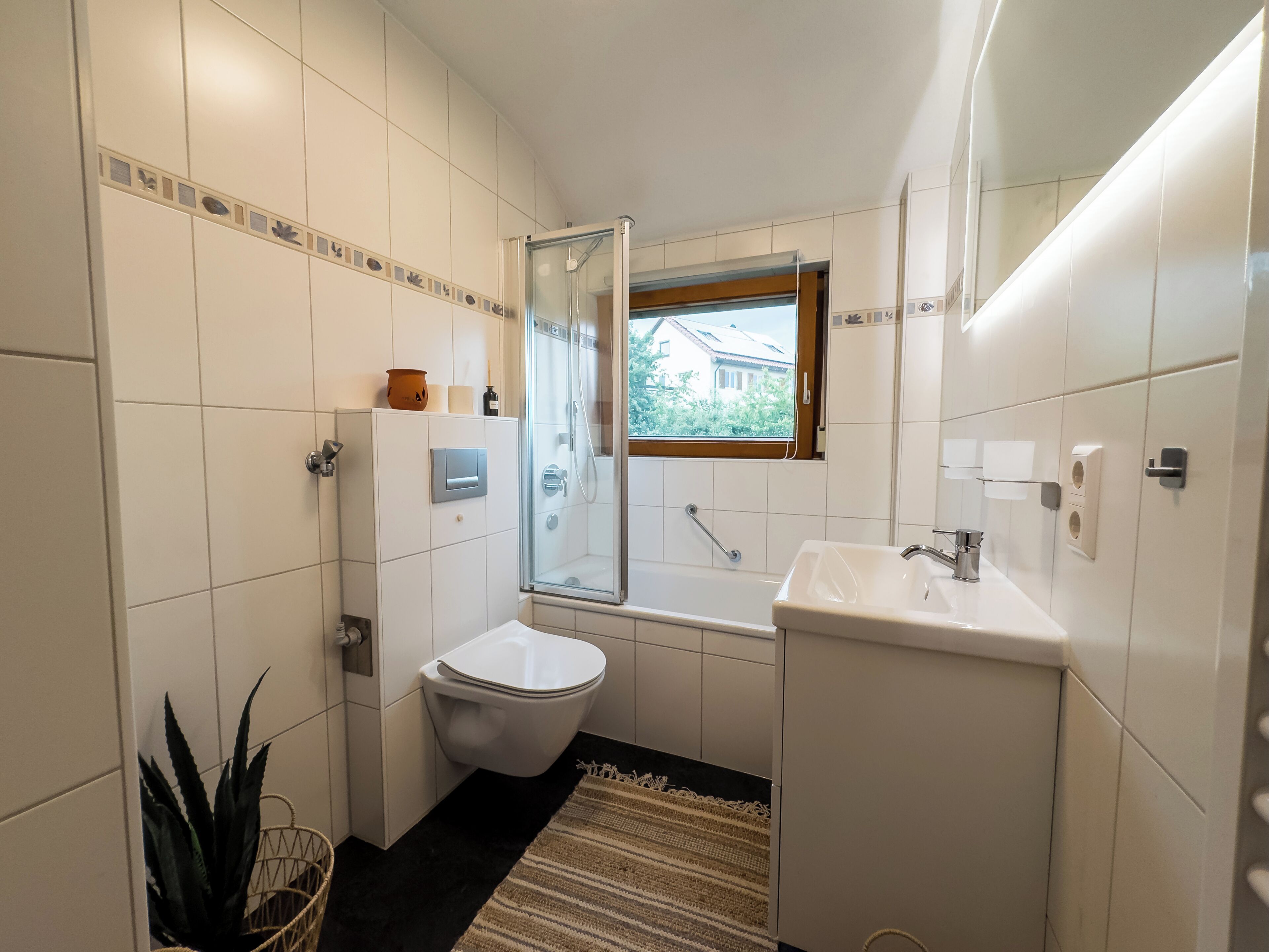 A compact bathroom with a toilet, a glass shower enclosure, a sink, and a small window.