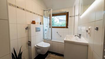 A compact bathroom with a toilet, a glass shower enclosure, a sink, and a small window.
