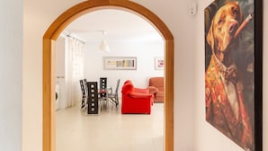 Un salon avec un canapé rouge, un coin repas avec des chaises et, au fond, une cuisine.
