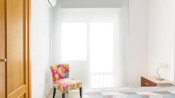 Un dormitorio con cama, una silla, una mesita de noche y una ventana.