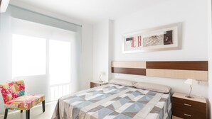 Une chambre à coucher comprenant un lit, des tables de chevet, une chaise et une œuvre d’art accrochée au mur.