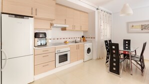 Une cuisine compacte équipée d’un réfrigérateur, d’un four, d’un four à micro-ondes et d’un lave-linge. On y trouve également une table à manger avec des chaises.
