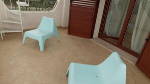 Ein Balkon mit zwei hellblauen Plastikstühlen, einem Metallgeländer und einer Holztür mit einem Insektengitter.