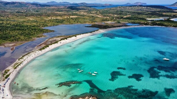 Luftaufnahme einer Küstenlandschaft mit klarem türkisblauem Wasser, einem Sandstrand und Booten.