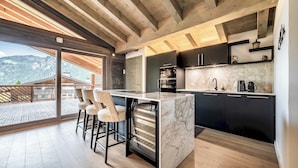 A modern kitchen with a marble countertop, black cabinets, and a large window overlooking a deck.