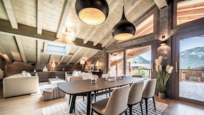 A spacious dining area with a wooden table and chairs, large windows offering mountain views, and a high ceiling with exposed beams.