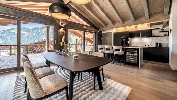A spacious dining area with a large table and chairs, a kitchen with modern appliances, and a view of the mountains through large windows.
