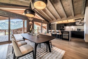 A spacious dining area with a large table and chairs, a kitchen with modern appliances, and a view of the mountains through large windows.