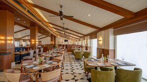 A spacious restaurant with high ceilings, wooden beams, and a checkered floor. Tables are set with chairs, and the room has large windows. - Radisson Resort Mount Abu (Mount Abu)