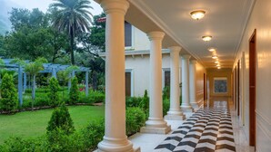 A corridor with white columns, a checkered floor, and a garden with greenery and a palm tree. - Radisson Resort Mount Abu (Mount Abu)
