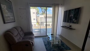 A living room with a sofa, a TV mounted on the wall, and a glass door leading to an outdoor area. - Tropical Getaway in Heredia, Costa Rica (Heredia)