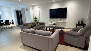 A modern living room with a grey sofa, a coffee table, and a flat-screen TV mounted on the wall. - Tropical Getaway in Heredia, Costa Rica (Heredia)