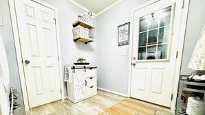 A hallway with two white doors, a white cabinet with drawers, a shelf with decorative items, a framed sign, and a woven rug on the floor. - 4BD | 3BTH | Pool | HotTub | Games |5Miles to I-95 (Elloree)