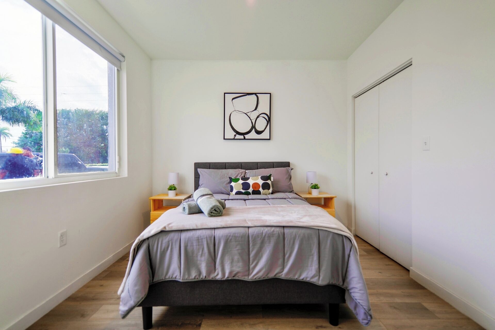 Un dormitorio con cama, ventana, una obra de arte en la pared y un armario.