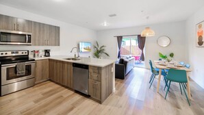 A modern kitchen with a microwave, stove, and dishwasher. There is a dining area with a table and chairs. - Contemporary Townhouse Close to Design District (North Miami Beach)