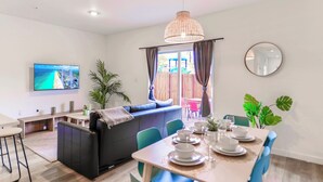 A modern living room with a sofa, dining table set for four, a TV, and a large window with curtains. - Contemporary Townhouse Close to Design District (North Miami Beach)