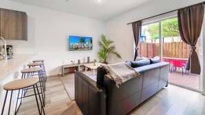 A modern living room with a sofa, a dining area with stools, a kitchen with a bar, and a large window with curtains. - Contemporary Townhouse Close to Design District (North Miami Beach)