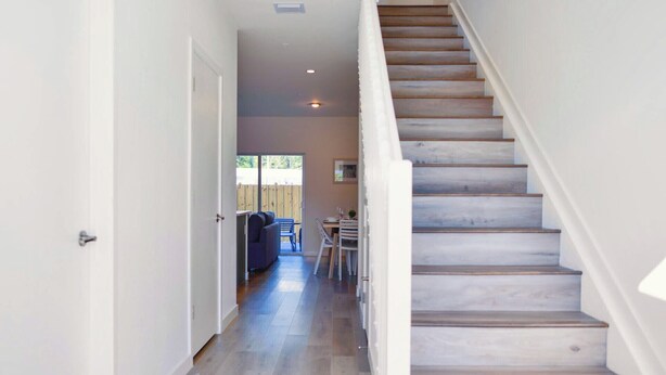 A staircase leading to a second floor with a wooden finish, a hallway with a door on the left, and a dining area with a table and chairs visible in the background. - Contemporary Townhouse Close to Design District (North Miami Beach)