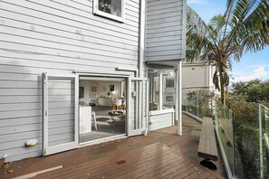 A modern house with a wooden deck, a glass door leading to an interior space with a dining area, and a view of a palm tree.