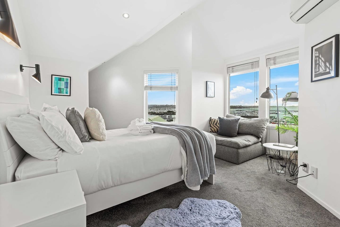 A modern bedroom with a bed, a sofa, a small table, and a view of the city.
