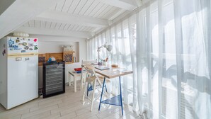 Une cuisine lumineuse équipée d’un réfrigérateur, d’un mini-réfrigérateur noir, d’une table en bois et d’une chaise.