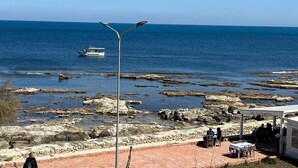 Une zone côtière au relief rocheux, un bateau sur l’eau et un bâtiment doté d’une terrasse.