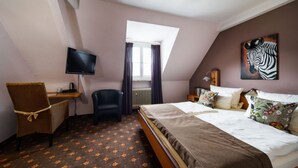 A bedroom with a bed, a desk, a chair, a television, a window with curtains, and a zebra painting on the wall. - Family-run hotel with a central location (Rüdesheim am Rhein)