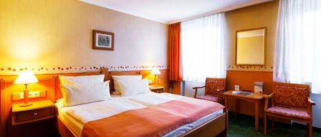A hotel room with a large bed, two bedside tables with lamps, a chair, a small table, and a mirror on the wall.