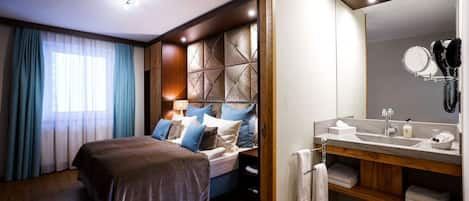 A modern hotel room with a large bed, a vanity with a mirror, and a wooden headboard.