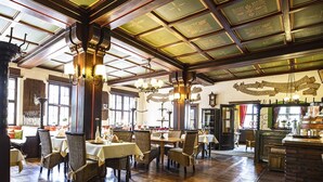 A spacious dining area with wooden flooring and high ceilings, featuring tables and chairs arranged for dining. - Family-run hotel with a central location (Rüdesheim am Rhein)