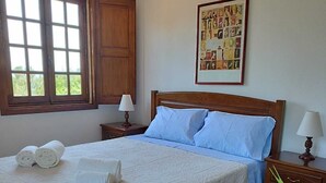 Un lit bien fait, recouvert d’une couvre-lit blanche et agrémenté d’oreillers bleus, avec une tête de lit en bois et un tableau encadré accroché au mur.
