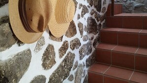 Un mur de pierre orné de deux chapeaux de paille, un escalier recouvert de carreaux rouges et, au fond, une bibliothèque.