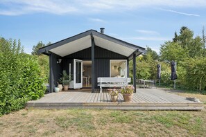 A modern outdoor structure with a covered patio, a white bench, and potted plants.