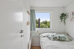 A small, single-room accommodation with a bed, a window with a view of greenery, a bedside table, and a radiator. - Holiday bliss near beach and nature (Græsted)