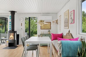 A cozy room with a white interior, a wooden floor, a dining table with chairs, a sofa with cushions, a wall-mounted clock, and a fireplace. - Holiday bliss near beach and nature (Græsted)