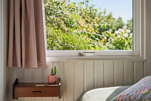 A bedroom with a window, a bedside table with a plant, and a bed with a floral bedspread. - Holiday bliss near beach and nature (Græsted)